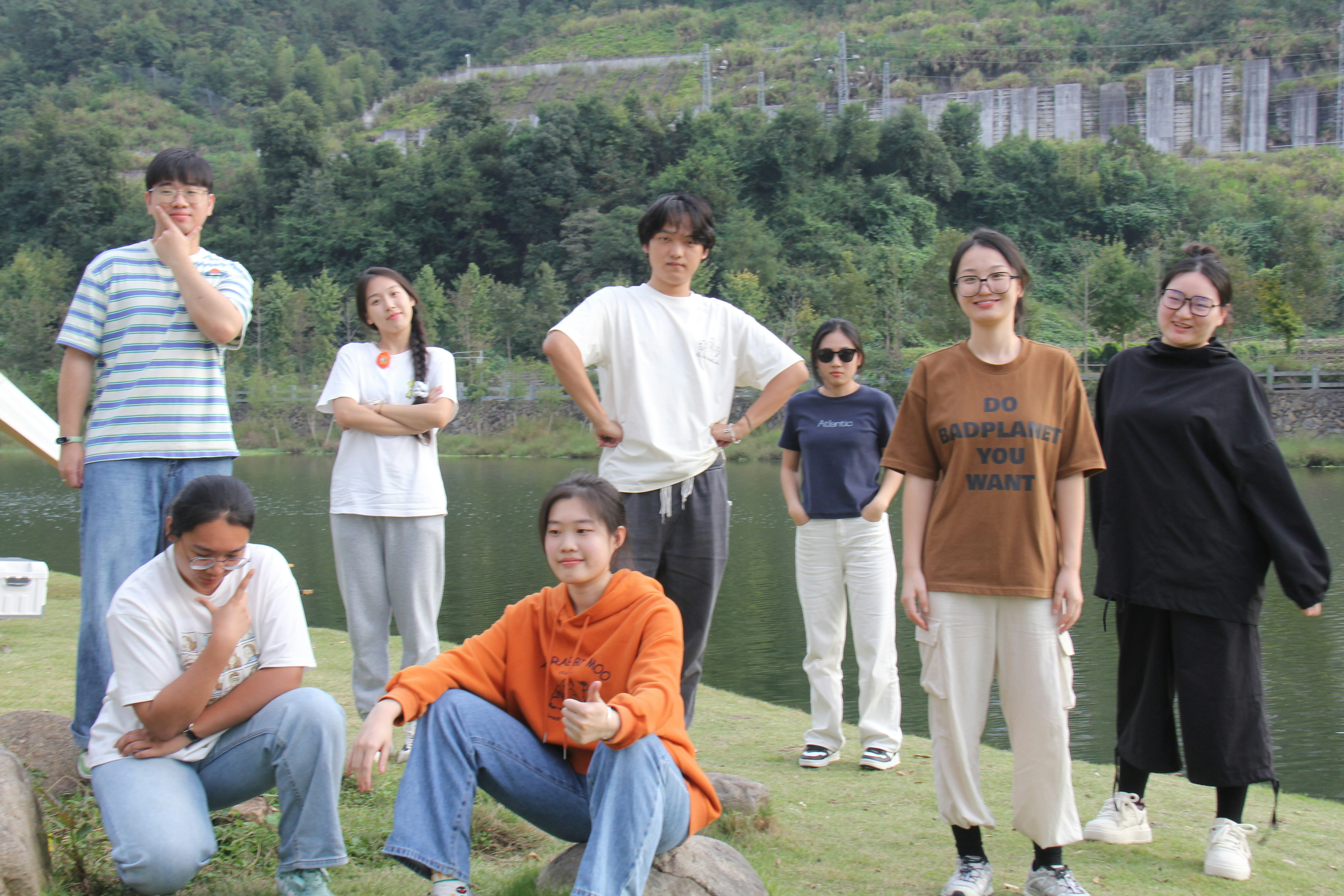 Eight young people posing outdoors by a lake